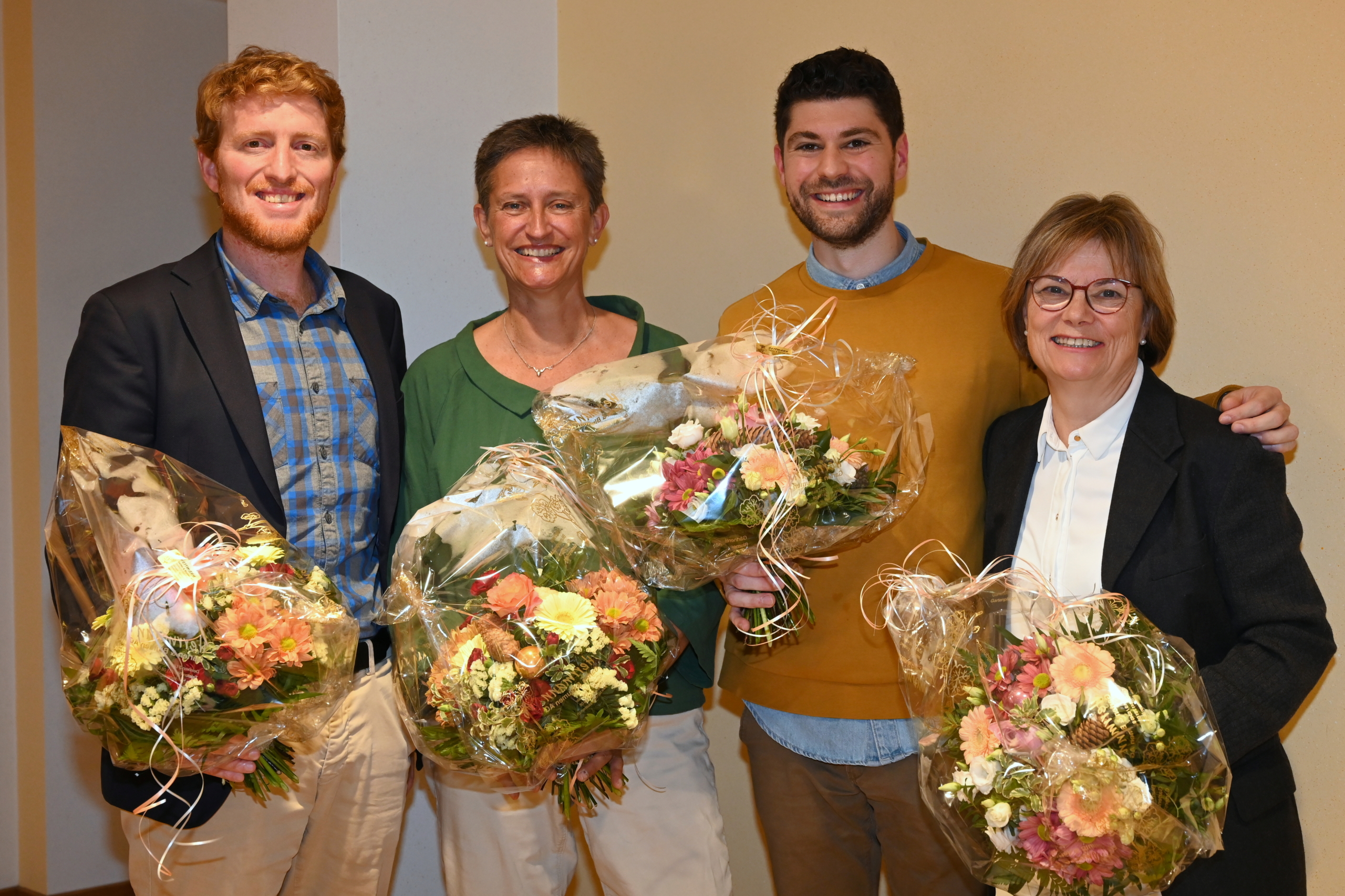 Das Alte Präsidium (ganz links Andreas Lustenberger und ganz rechts Esther Haas) mit dem neuen Co-Präsidium der Alternativen - die Grünen Kanton Zug: Mitte-links Trix Gubser, Mitte-rechts Luzian Franzini. Alle vier sind festlich gekleidet und halten ein grosses Blumenbouquet.